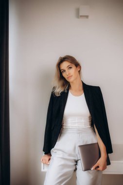 Ofisinde dizüstü bilgisayarı olan siyah ceketli bir sarışın..