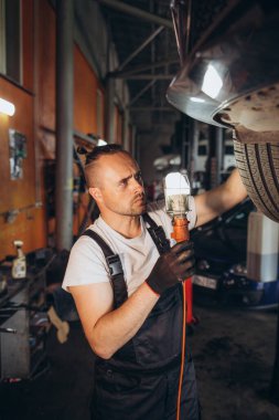 Detaylı bir inceleme. Elinde lamba olan sakallı genç adam kaldırılmış arabanın altını dikkatle inceliyor. Yüksek kalite fotoğraf