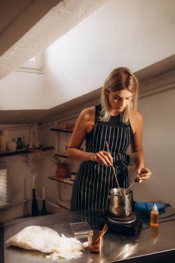 Güzel genç bir kadın vegan ve organik mum yapmak için soya cilasını eritiyor. Ekolojik ve vejetaryen işleri. Mum aksesuarları. Sevgiyle el yapımı. Uzak çalışma, çevrimiçi dükkan, işyeri