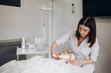 Kozmetik uzmanı yüz tedavisi yapıyor ve yüz maskesi takıyor. Yüksek kalite fotoğraf