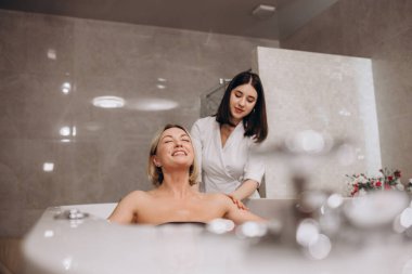 Güzellik salonunda hidromasaj yaparken genç bir kadın. Vücut bakımı ve kaplıca kavramı. Masöz, banyodaki kıza bir su püskürtüsüyle masaj yapar. Yüksek kalite fotoğraf