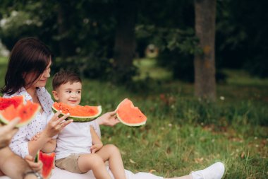 Anne ve genç oğlu çimenlerin üzerinde oynadı. Karpuz yeme anne ve genç oğlu. Piknik. Yaz. 