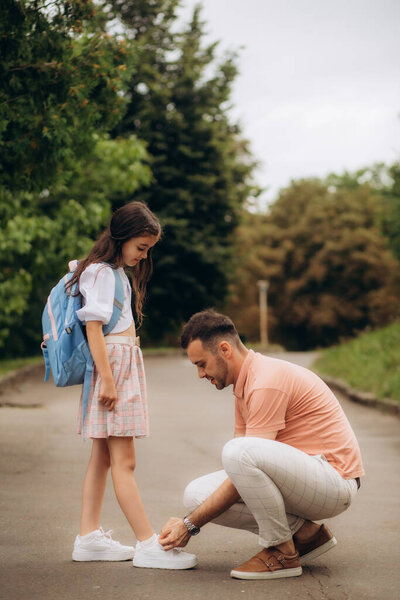 little girl is going to school. Dad ties his daughter's shoes.