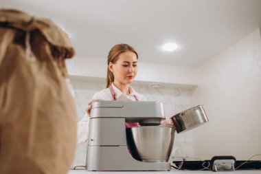 Güzel, genç, esmer pasta şefi kadın mutfakta hamur işleri pişiriyor neşeli bir şekilde sunum yapıyor ve avuç içi kameraya bakıyor. - Evet. Yüksek kalite fotoğraf