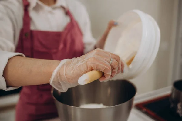 Close up photo of female confectioner mixes a fresh cream in deep plate with a kitchen mixer. The concept of homemade pastry, cooking. Confectioner makes a blender a cream for a cake in the kitchen.
