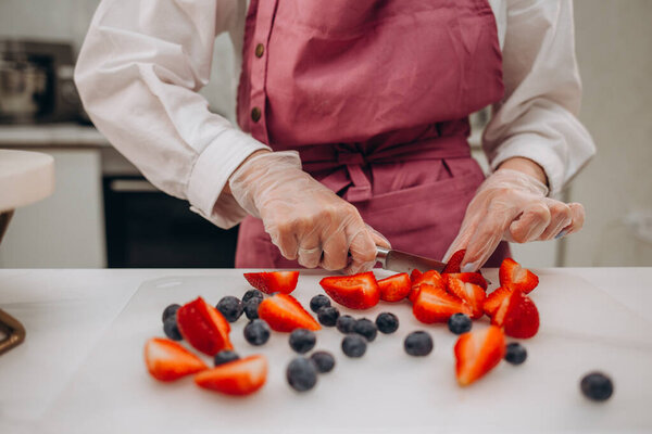 Woman confectioner in an apron decorating a cherry cake with cherries, a Homemade birthday cake. Summer fruit cake, vegan dessert, Selective focus. High quality photo