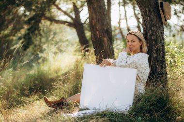 Yaşlı bir kadın, nehrin kenarındaki yağlı boya tablosunda bir resim çiziyor. Yüksek kalite fotoğraf