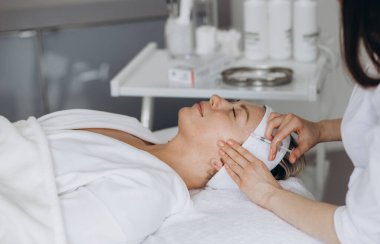 Doktor kozmetik uzmanı, güzellik salonundaki genç ve güzel bir kadının cildindeki kırışıklıkları sıkılaştırmak ve düzleştirmek için canlandırıcı yüz enjeksiyonu prosedürünü uyguluyor. Kozmetoloji, cilt bakımı. Yüksek kalite fotoğraf