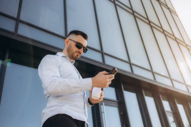 İş, teknoloji ve insan kavramı. Akıllı telefonlu genç adam kahve içiyor ve sokak kafesinde mesajlaşıyor. Yüksek kalite fotoğraf