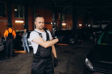Yakışıklı Gülümseyen Araba Machanic Garajda duruyor. Otomobilin Önünde Çapraz Kollu Siyah Üniformalı Kafkas Yetişkin Teknisyen Ustasının Portresi. Araba servisi konsepti onarılıyor. Yüksek kalite fotoğraf