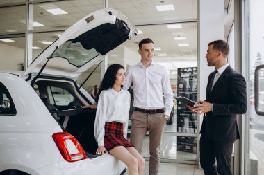 Genç çift başarılı araba satın alma sonra satış temsilcisi ile tokalaşırken. 