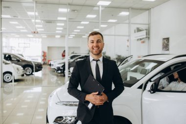 Kendine güveni tam beyaz bir erkek mağaza asistanının resmi kıyafetleriyle otomobil galerisindeki kameraya bakarken yakın plan çekimi. Yüksek kalite fotoğraf