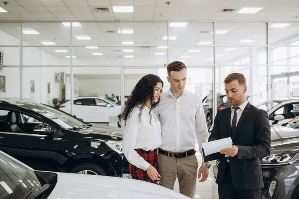 Couple and the dealer selling cars look the car in the showroom. High quality photo