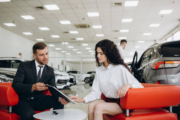 Пара и дилер, продающий машины, смотрят на машину в выставочном зале. Высокое качество фото