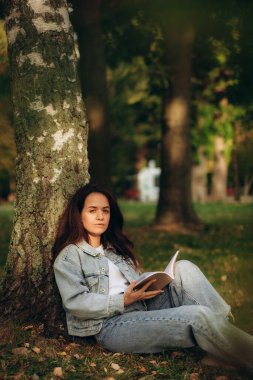 Akşam güneşinde piknik sırasında ağacın altında kitap okuyan genç bir kadın. Yüksek kalite fotoğraf