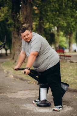 Şişman adam sırtını parktaki spor sahasında sallıyor.