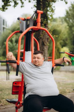 Şişman bir adam parkta spor yaparak kilo veriyor.