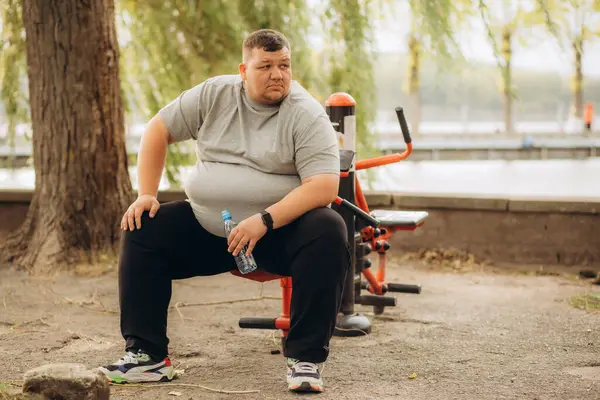 One tired young overweight man sitting down at park bench to rest. A fat person resting outdoors. High quality photo