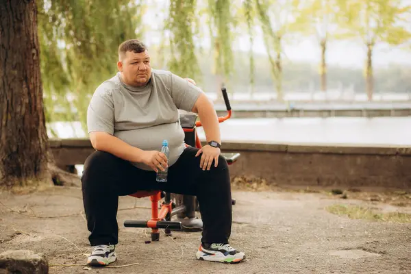 One tired young overweight man sitting down at park bench to rest. A fat person resting outdoors. High quality photo