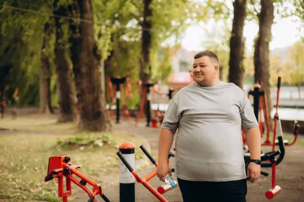 Şişman bir adam parkta spor yapıyor.