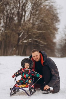 Yakışıklı genç baba ve küçük tatlı kızı kışın dışarıda eğleniyorlar. Kızak sürerken birlikte vakit geçirmenin tadını çıkarıyorum. Aile kavramı. Yüksek kalite fotoğraf