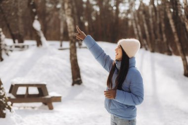 Kışın kalın elbiseli bir kadının portresi, soğuk bir kış gününde sıcak tutmak için kollarında nefes alan bir kadın, açık havada güzel genç bir kadın. Soğuk hava konsepti, donmuş eller. Yüksek kalite fotoğraf