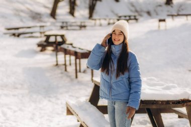 Mavi ceketli genç bir kadın kış parkında telefonla konuşuyor.