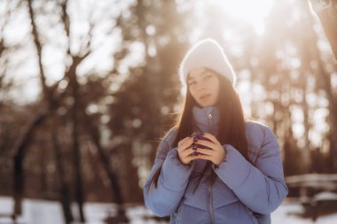 Kız kar yağmasından hoşlanıyor. Örgü şeklinde genç bir kadın, kar yağarken ormanda çay içiyor. Tonlu fotoğraf. Yüksek kalite fotoğraf