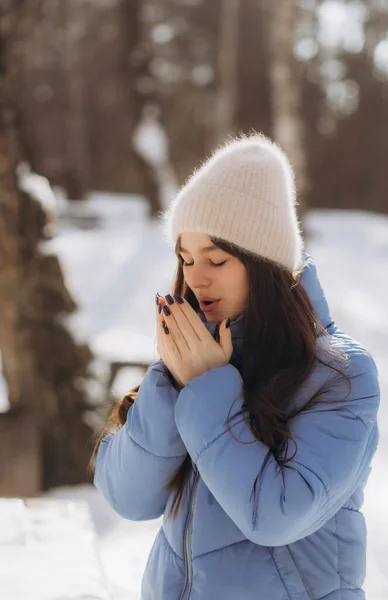Young girl breathes on her hands to keep warm at cold winter day. Girl warms her hands with a warm breath. High quality photo