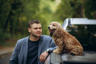 Bir adam, sonbahar ormanında bir cipin üstünde cocker spaniel köpeğiyle yürüyor.