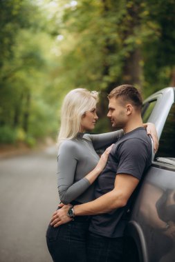 Mutlu çift cocker spaniel köpeğiyle sonbahar ormanında cipin kaputunda oturuyor.