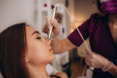 Kozmetik uzmanı, pigmentasyondaki kızın yüzünü lazerle temizliyor. Donanım tedavisi. Dermatoloji kliniğindeki kızın yüzündeki kan damarlarının lazerle alınması. Yüksek kalite fotoğraf