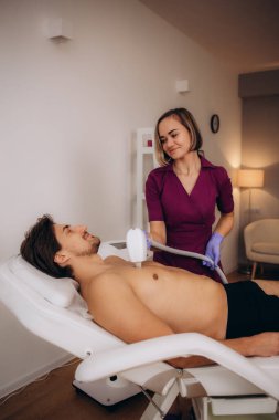 Güzellik salonundaki kendine güvenen sakallı adam. Erkekler, özel lazer teçhizatıyla göğüs kıllarının alınması için prosedürü uygularlar. Yüksek kalite fotoğraf