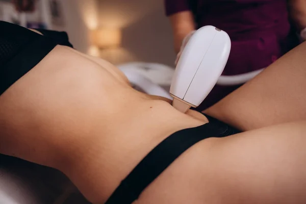 Professional beautician removes hair on beautiful female tummy using a laser. hair removal on the belly, laser procedure at clinic. High quality photo