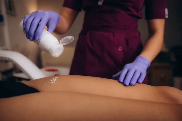 Cosmetologist sprinkling talcum powder on woman leg before the depilation procedure over white background. High quality photo