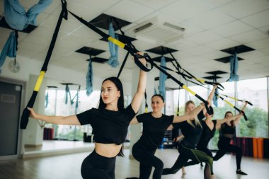 Spor salonunda yoga yapan gülümseyen beş kızdan oluşan bir grup. Spor salonundaki paspasların üzerinde elleri havada esneyen, büyük pencereli, aynalı, tavan arası kaplamalı genç kadınlar. Sağlıklı yaşam tarzı kavramı. Yüksek kalite fotoğraf