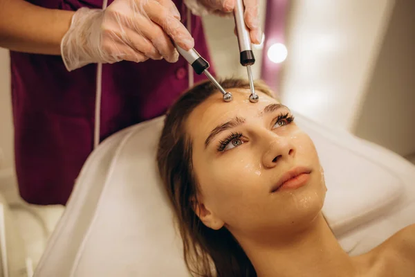 stock image A doctor cosmetologist makes a microcurrent facial therapy to a young woman with a device in a beauty wellness salon.Cosmetology and professional skin care. High quality photo
