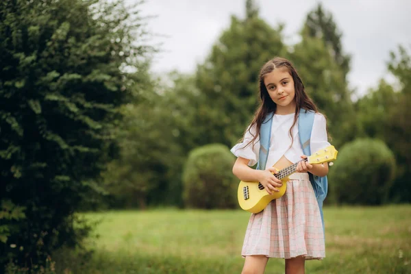 Little girl playing guitar in the field at sunset. Portrait of child and guitar. High quality photo