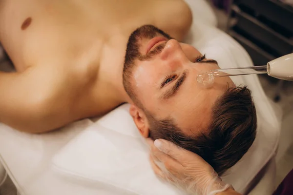 Darsonval yüz terapisi. Genç adam, güzellik kliniği. Cilt esnekliğini arttırmanın yolları. Yüksek kalite fotoğraf