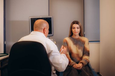 Bir doktor modern bir klinikte arka planda bulunan bir hastaya tiroid bezinin ultrasonunu ve servikal lenf nodlarını uygular. Modern tıp ve teknolojinin reklamı. Yüksek kalite fotoğraf