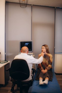 Bir doktor modern bir klinikte arka planda bulunan bir hastaya tiroid bezinin ultrasonunu ve servikal lenf nodlarını uygular. Modern tıp ve teknolojinin reklamı. Yüksek kalite fotoğraf