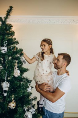 Noel ağacı süslemek. Omuzlarında kızıyla genç bir adam Noel ağacını süslemesine yardım ediyor..