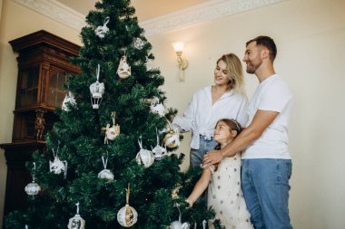 Noel ağacı süslemek. Omuzlarında kızıyla genç bir adam Noel ağacını süslemesine yardım ediyor..