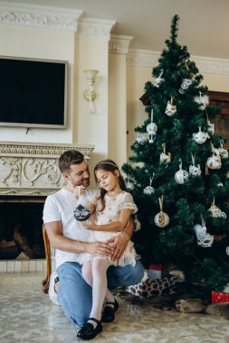Noel ağacı süslemek. Omuzlarında kızıyla genç bir adam Noel ağacını süslemesine yardım ediyor..