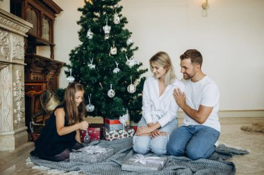 Mutlu Noeller ve mutlu tatiller. Neşeli anne ve tatlı kızları birbirlerine hediye veriyorlar. Ebeveynler ve iki küçük çocuk içeride Noel ağacının yanında eğleniyor ve oyun oynuyorlar..