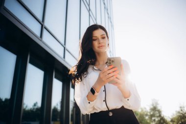 Arka planda ofis binaları olan caddede cep telefonuyla çalışan bir yönetici. Yüksek kalite fotoğraf