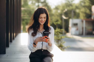 Sokakta akıllı telefon kullanan Kafkasyalı bir iş kadını. Kahve molasında ofis binasının yakınında mesaj yazan güzel bir kadın.