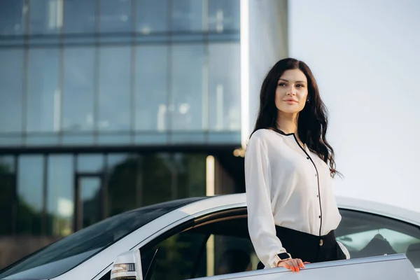 Nice business woman calling client on smartphone, standing near automobile. High quality photo