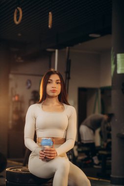 Seksi, formda bir kızın spor salonunda oturup su içtiği bir resim.. 