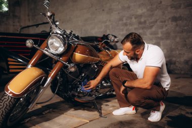 Bir adam garajında eski motosikletleri ve eski arabaları topluyor.